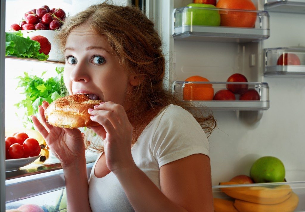 woman eats sweets at night to sneak in a refrigerator