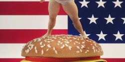 Fat man standing on a hamburger with the USA flag background.