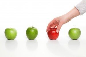 Hand picking red apple among green apples