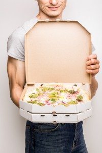 Pizza delivery courier. Young caucasian man holds open box with pizza carbonara