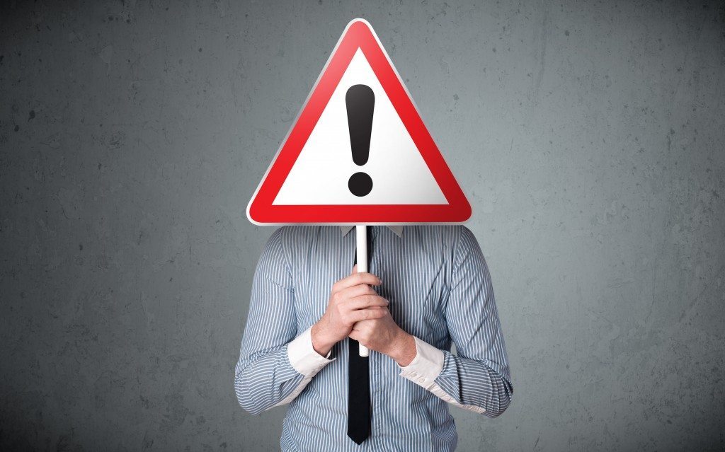 Businessman holding a red traffic triangle warning sign in front of his head